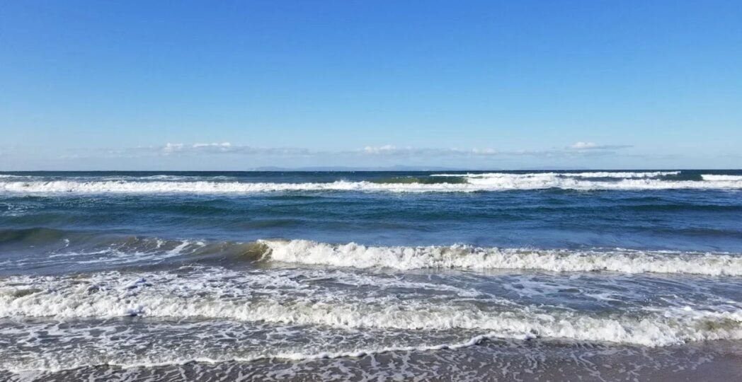 Waves rolling onto the sandy shore under a clear blue sky at a peaceful beach.