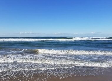 Waves rolling onto the sandy shore under a clear blue sky at a peaceful beach.