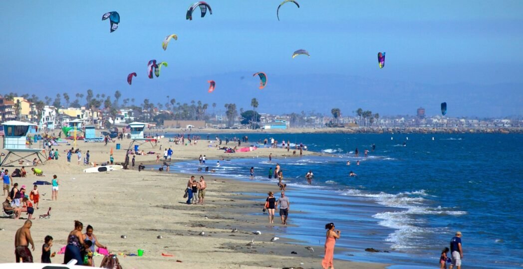 People enjoying the sunny beach with colorful kites in the sky at Long Beach, California