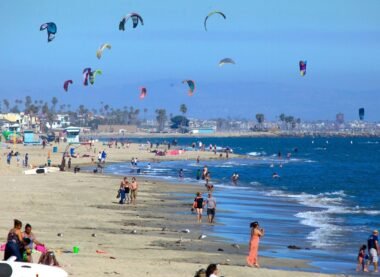 People enjoying the sunny beach with colorful kites in the sky at Long Beach, California
