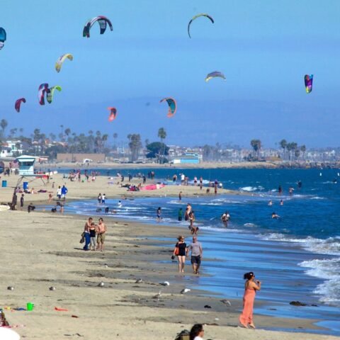 People enjoying the sunny beach with colorful kites in the sky at Long Beach, California