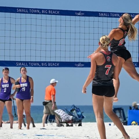 Beach volleyball tournament beside the ocean with athletes competing on sandy courts during a sunny coastal sports event.